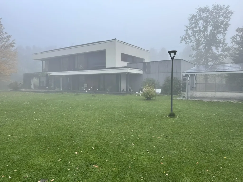 Modernistyczny dom dwukondygnacyjny w jesiennej mgle, duży ogród trawiasty, latarnia parkowa, w tle carport z fotowoltaiką