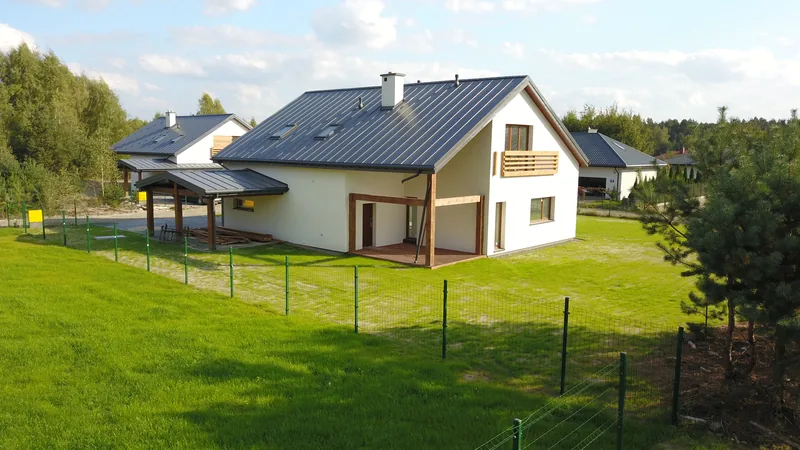 Drone shot wykończonego domu jednorodzinnego z grafitowym dachem, drewnianymi tarasami i ogrodzeniem