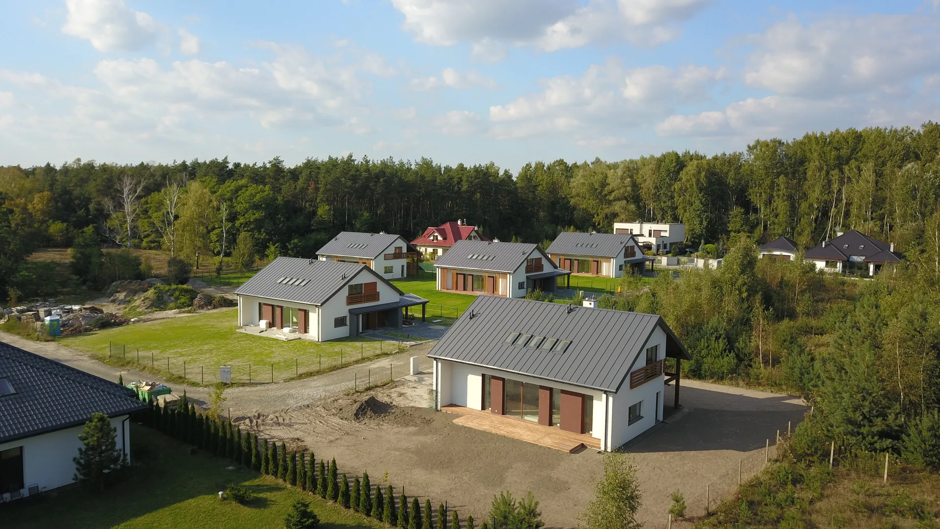Drone shot osiedla siedmiu domów jednorodzinnych w otoczeniu lasu, czerwone i grafitowe dachy, jesienne światło