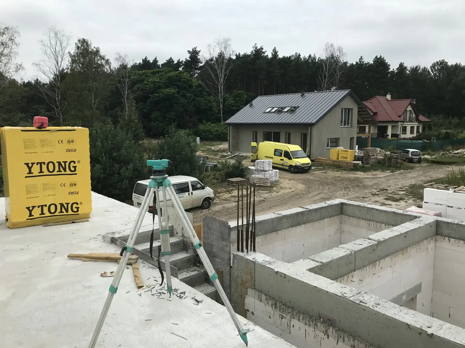 Niwelator geodezyjny na statywie na płycie fundamentowej, materiały YTONG i van na placu budowy, etap pomiarów